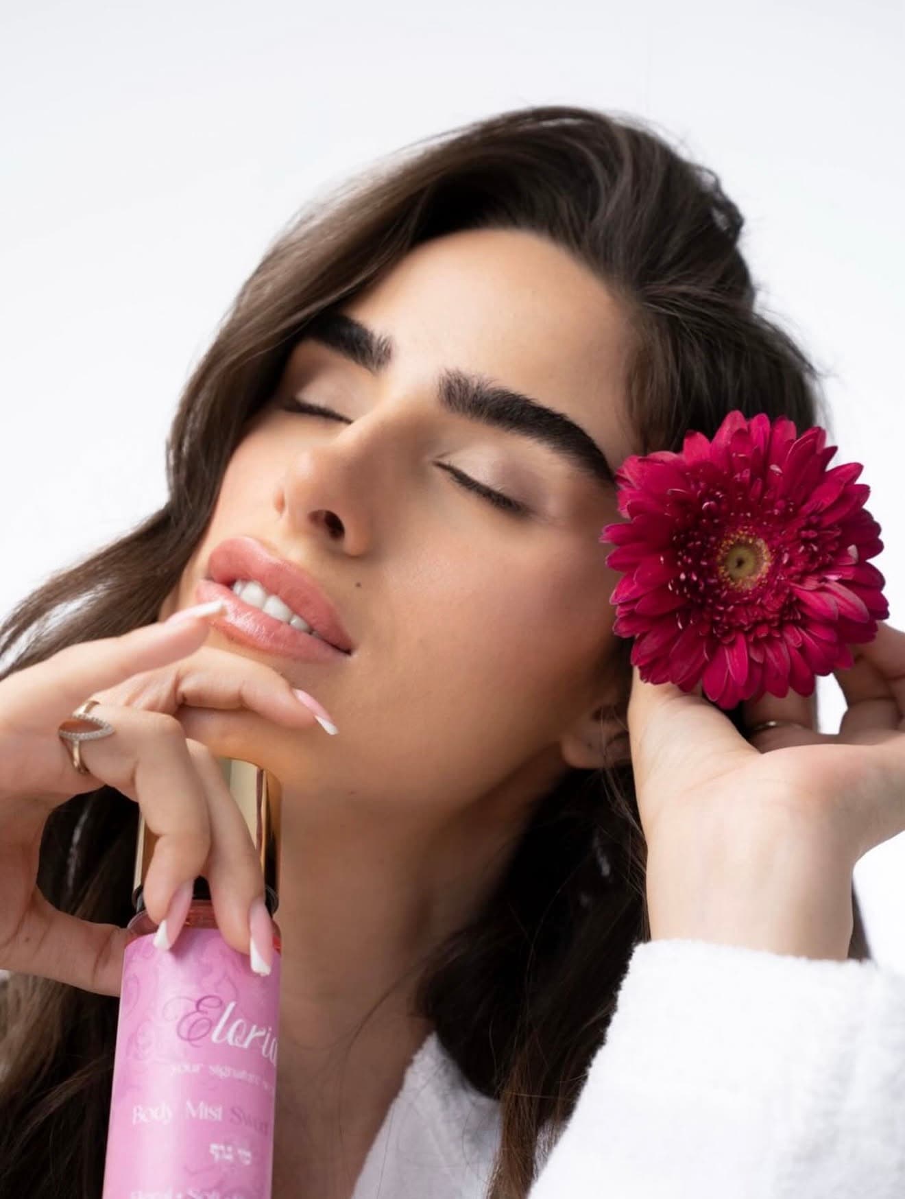 אישה עטופה בחלוק מחזיקה מוצרי טיפוח של Eloria
